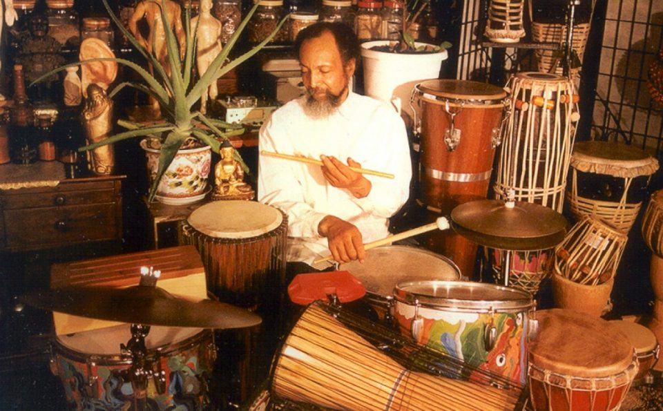 portrait of Milford Graves surrounded by and playing various types of drums